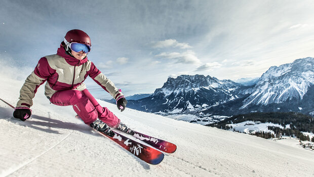 Skifahrerin in pinker Skibekleidung fährt in sportlicher Haltung eine Kurve auf einer verschneiten Piste.